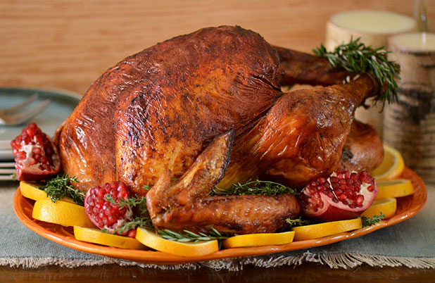 A whole roasted turkey on a bed of oranges, pomegranates, rosemary and an orange platter.